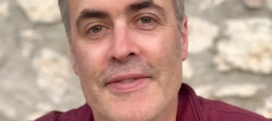 Donal O'Carroll is smiling at the camera, wearing a red shirt. He's in front of a stone wall