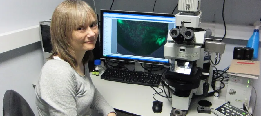 Image of Professor Val Wilson sat at a desk with a computer and microscope