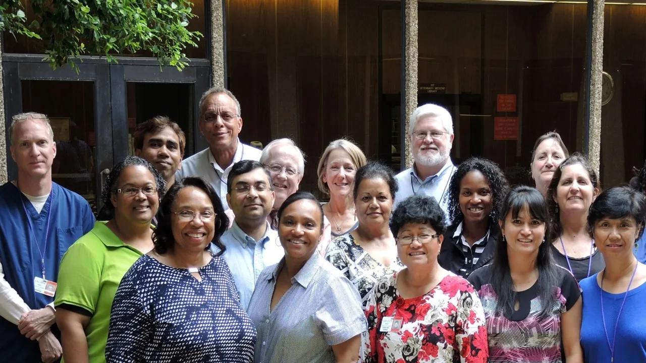 A group of 17 researchers stand in front of a dark building, smiling at the camera